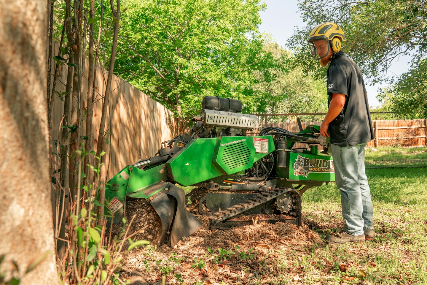 Worker in a yellow hard hat operates a stump grinder.